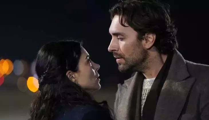 A man and woman face each other closely at night, about to kiss, with blurred city lights behind them.