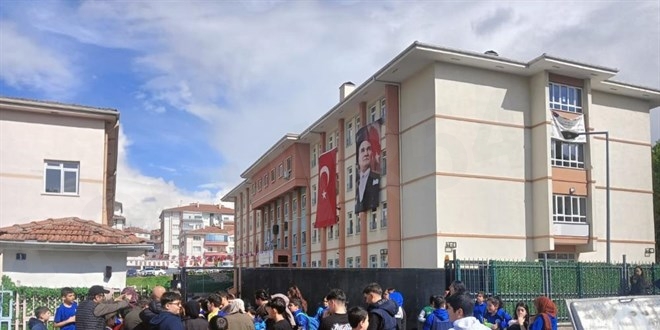 Group of students gathered outside a beige multi-story campus building with Turkish flags and banners hanging from the facade.