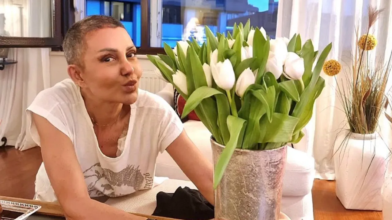 Person with short hair leaning toward a bouquet of white tulips in a metal vase on a wooden table indoors, making a kissy face at the camera.