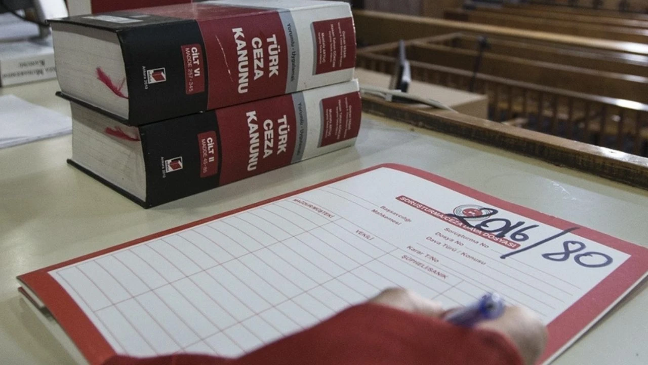 Two Turkish Penal Code books stacked on a desk beside a person writing on a red-bordered form or sheet.